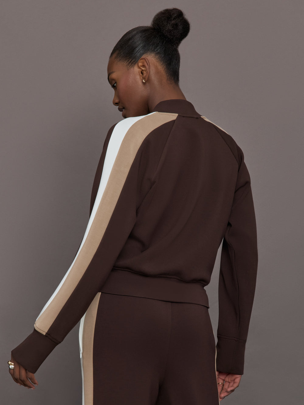 Model wearing brown bomber with white and beige stripes on the sleeves.