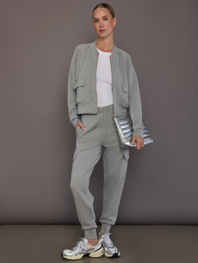 Model is wearing a matching set in heather grey ultrasoft fabric featuring the bomber jacket and cargo jogger, styled with a white ribbed tank top, silver sneakers, and a metallic clutch, full front view.