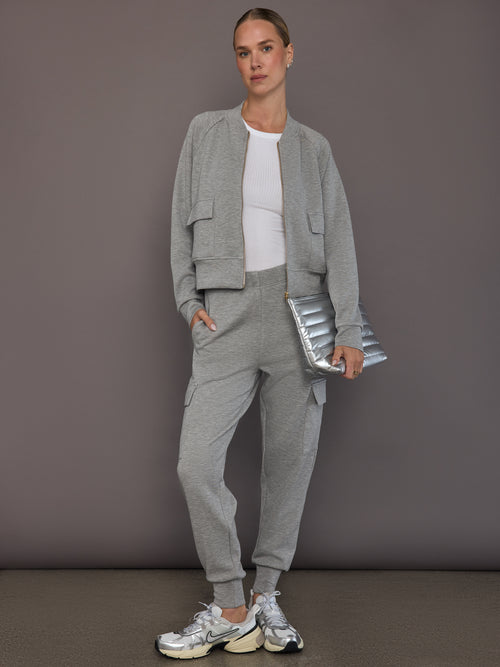 Model is wearing a matching set in heather grey ultrasoft fabric featuring the bomber jacket and cargo jogger, styled with a white ribbed tank top, silver sneakers, and a metallic clutch, full front view.