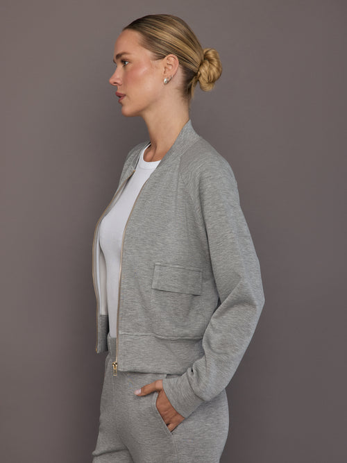 Model is wearing a heather grey Ultrasoft Bomber Jacket with gold zipper and front pocket detail, side view.