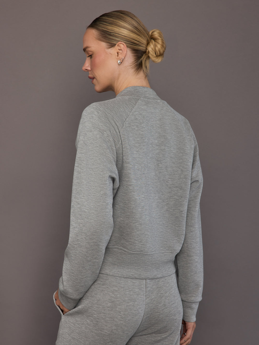 Model is wearing a heather grey Ultrasoft Bomber Jacket with clean straight hem and raglan sleeve construction, back view.