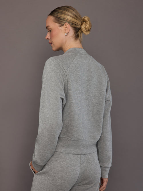 Model is wearing a heather grey Ultrasoft Bomber Jacket with clean straight hem and raglan sleeve construction, back view.