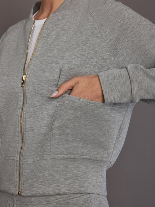 Close-up of the heather grey Ultrasoft Bomber Jacket showing gold zipper and front utility pocket detail.