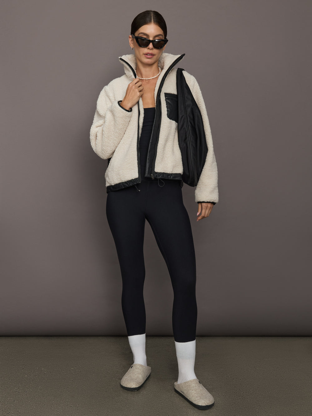 Model styled in Faux Leather Sherpa Jacket in nude sherpa with black trim, paired with leggings, sunglasses, and slippers.