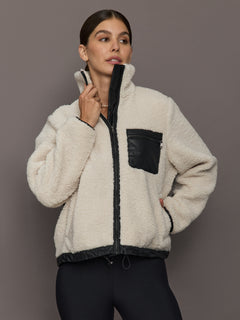 Model wearing Faux Leather Sherpa Jacket in natural sherpa with black faux leather trim and chest pocket, front view.