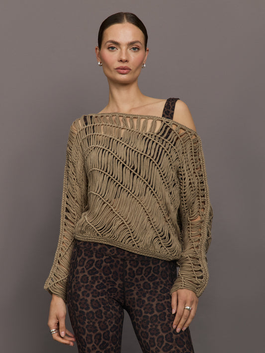 Model wears a crocheted one shoulder sweater in light brown.