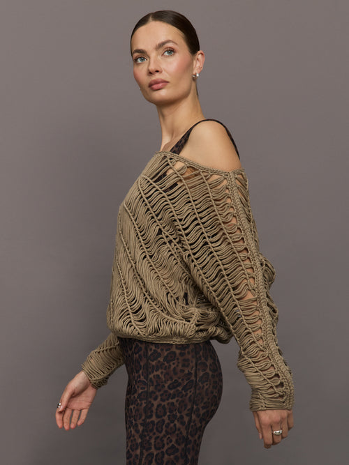 Model wears a crocheted one shoulder sweater in light brown.