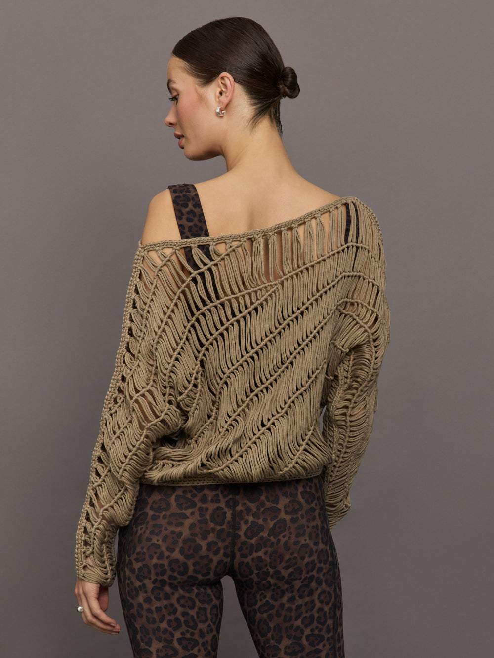Model wears a crocheted one shoulder sweater in light brown.