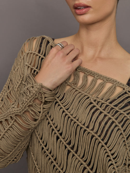 Model wears a crocheted one shoulder sweater in light brown.
