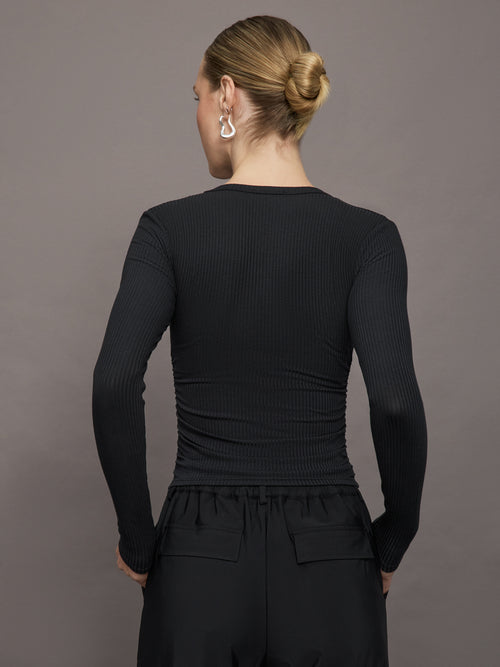 Model wears a ribbed jersey fitted long sleeved black top with ruching down both sides. 