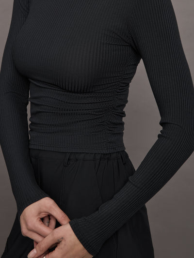 Model wears a ribbed jersey fitted long sleeved black top with ruching down both sides. 