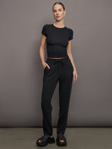 Model wears a short sleeved, ribbed jersey fitted black top with ruching down both sides. 