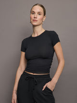 Model wears a short sleeved, ribbed jersey fitted black top with ruching down both sides. 