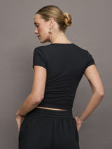 Model wears a short sleeved, ribbed jersey fitted black top with ruching down both sides. 