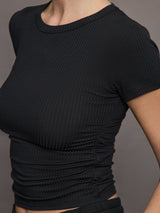 Model wears a short sleeved, ribbed jersey fitted black top with ruching down both sides. 