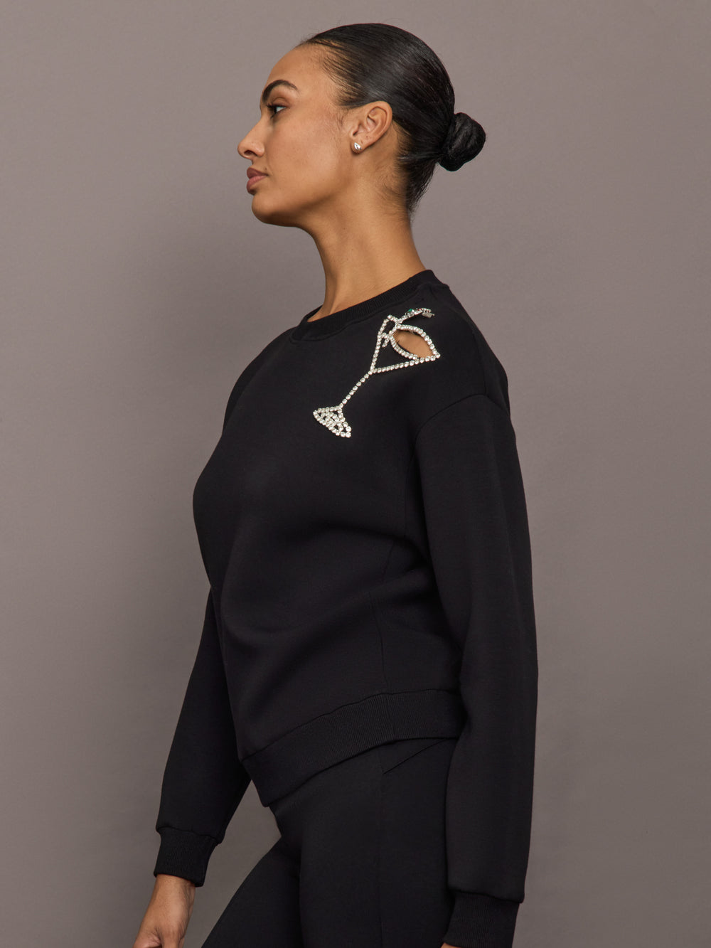 Side profile of model wearing black martini embellished sweatshirt with shoulder crystal martini glass detail.