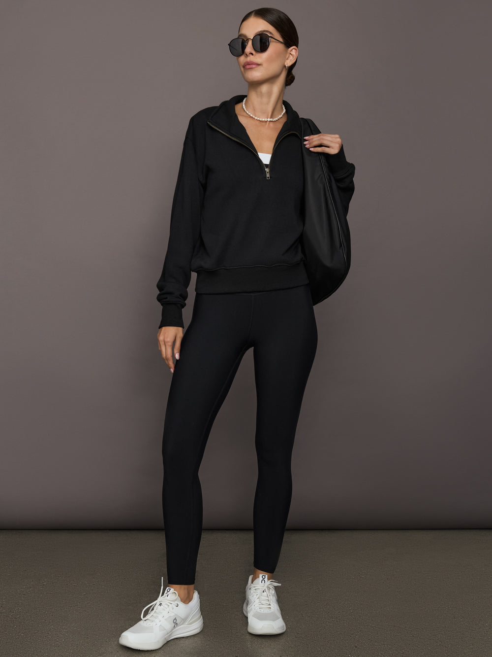 Model is wearing the Half Zip Fleece Top in black styled with black leggings, white sneakers, oversized black shoulder bag, and sunglasses, full front view.