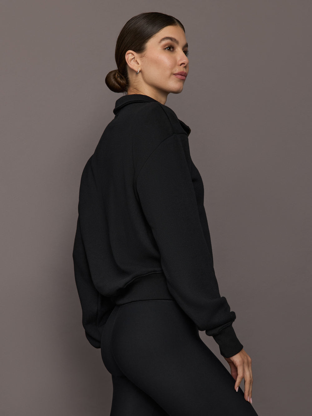 Model is wearing the Half Zip Fleece Top in black with ribbed hem and relaxed fit, back side view.