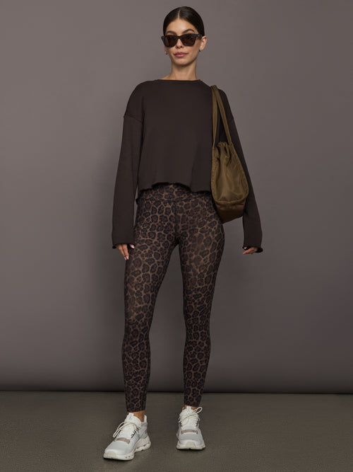 Model is wearing a dark brown crew sweatshirt styled with leopard print leggings, white sneakers, and a beige shoulder bag, full front view.