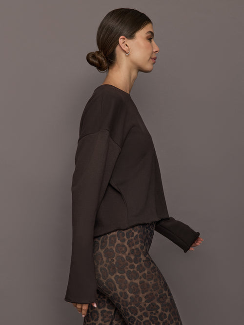 Model is wearing a dark brown crew sweatshirt with dropped shoulders, styled with leopard print leggings, side view.