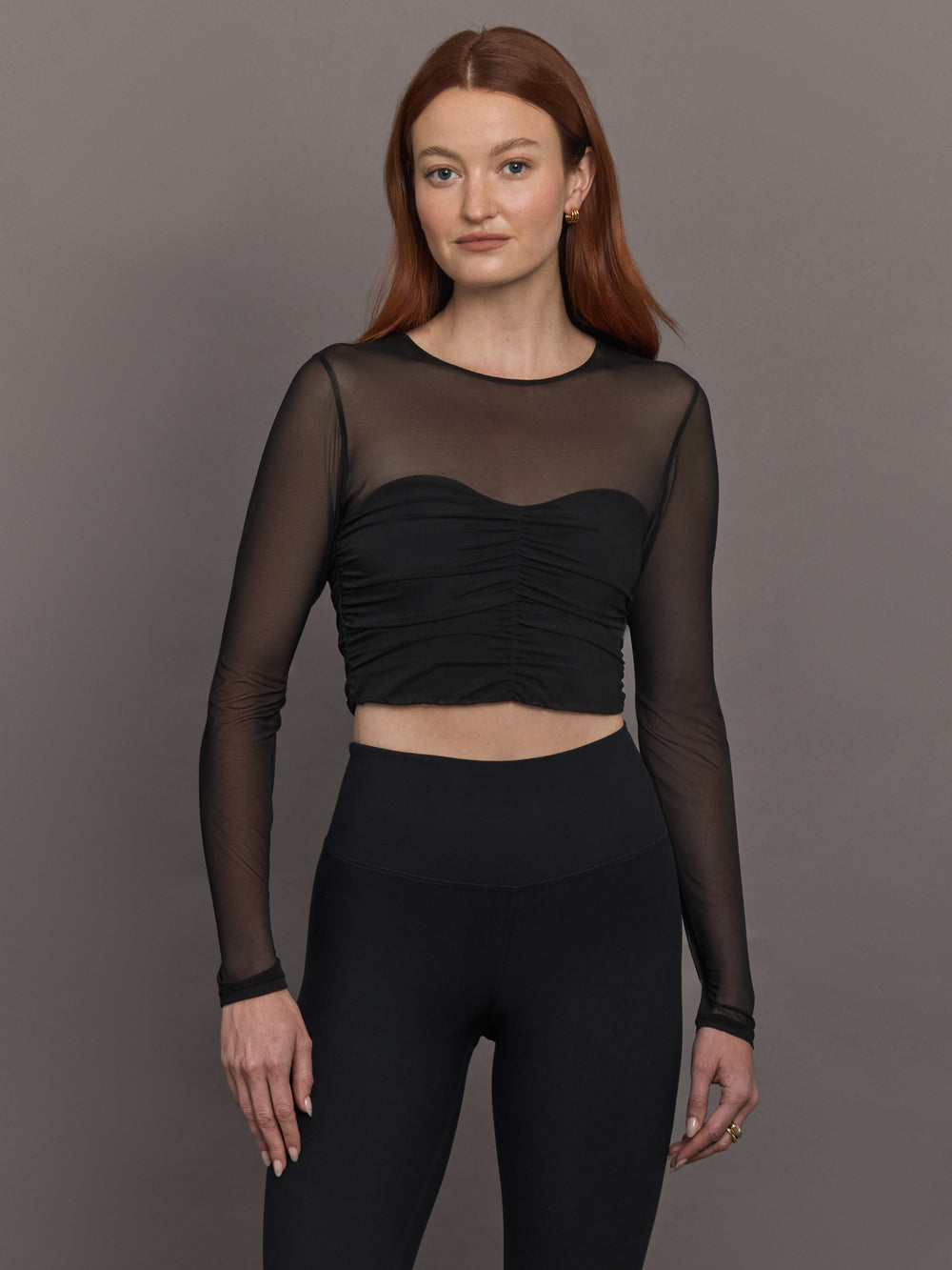 Model wears the The Melt and Mesh Ruched Top in Black, with a ruched center front, mesh on the sleeves and upper chest, and is cropped.