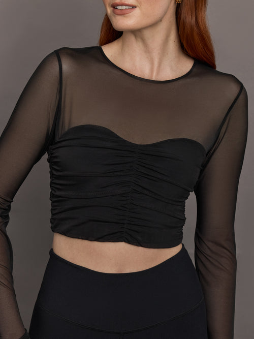 Model wears the The Melt and Mesh Ruched Top in Black, with a ruched center front, mesh on the sleeves and upper chest, and is cropped.