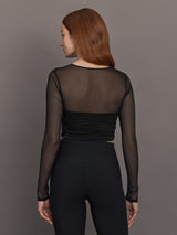 Model wears the The Melt and Mesh Ruched Top in Black, with a ruched center front, mesh on the sleeves and upper chest, and is cropped.