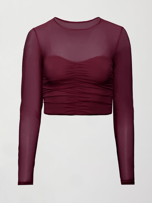 Model wearing a burgundy long sleeve top with sheer sleeves