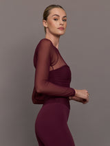Model wearing a burgundy long sleeve top with sheer sleeves
