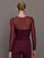 Model wearing a burgundy long sleeve top with sheer sleeves