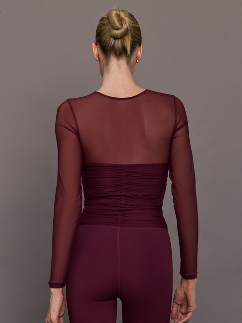 Model wearing a burgundy long sleeve top with sheer sleeves