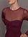 Model wearing a burgundy long sleeve top with sheer sleeves