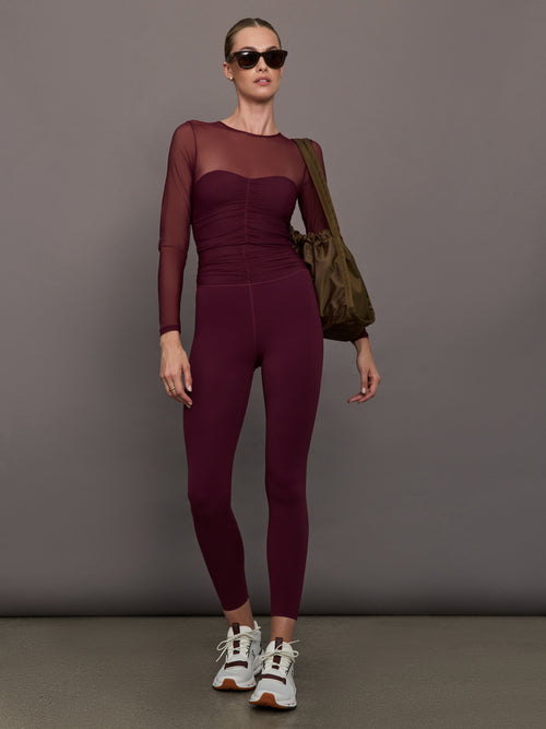 Model wearing a burgundy long sleeve top with sheer sleeves