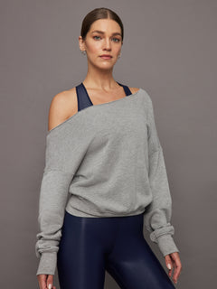 Model wears a grey, slouchy French terry sweatshirt with an off-the-shoulder, raw-edged asymmetrical neckline and a loose, relaxed fit.




