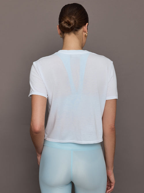 Model wears a cropped boxy white sheer tee shirt. 