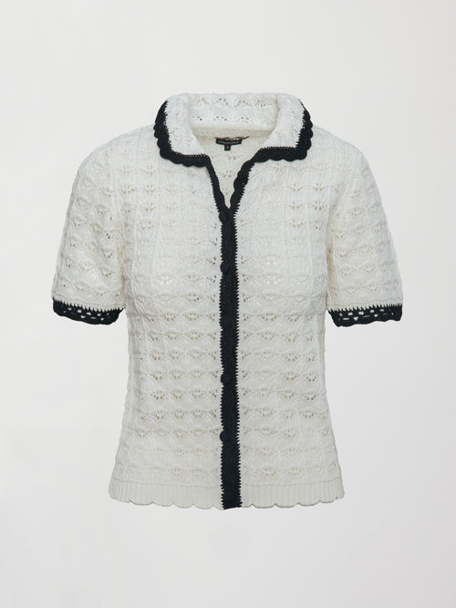 Model wears white and black crochet button-down top with short sleeves and a collared neck.