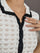 Model wears white and black crochet button-down top with short sleeves and a collared neck.