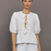 Model wears white puff sleeve top with a front ties and high neckline.





