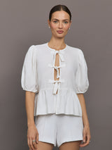 Model wears white puff sleeve top with a front ties and high neckline.





