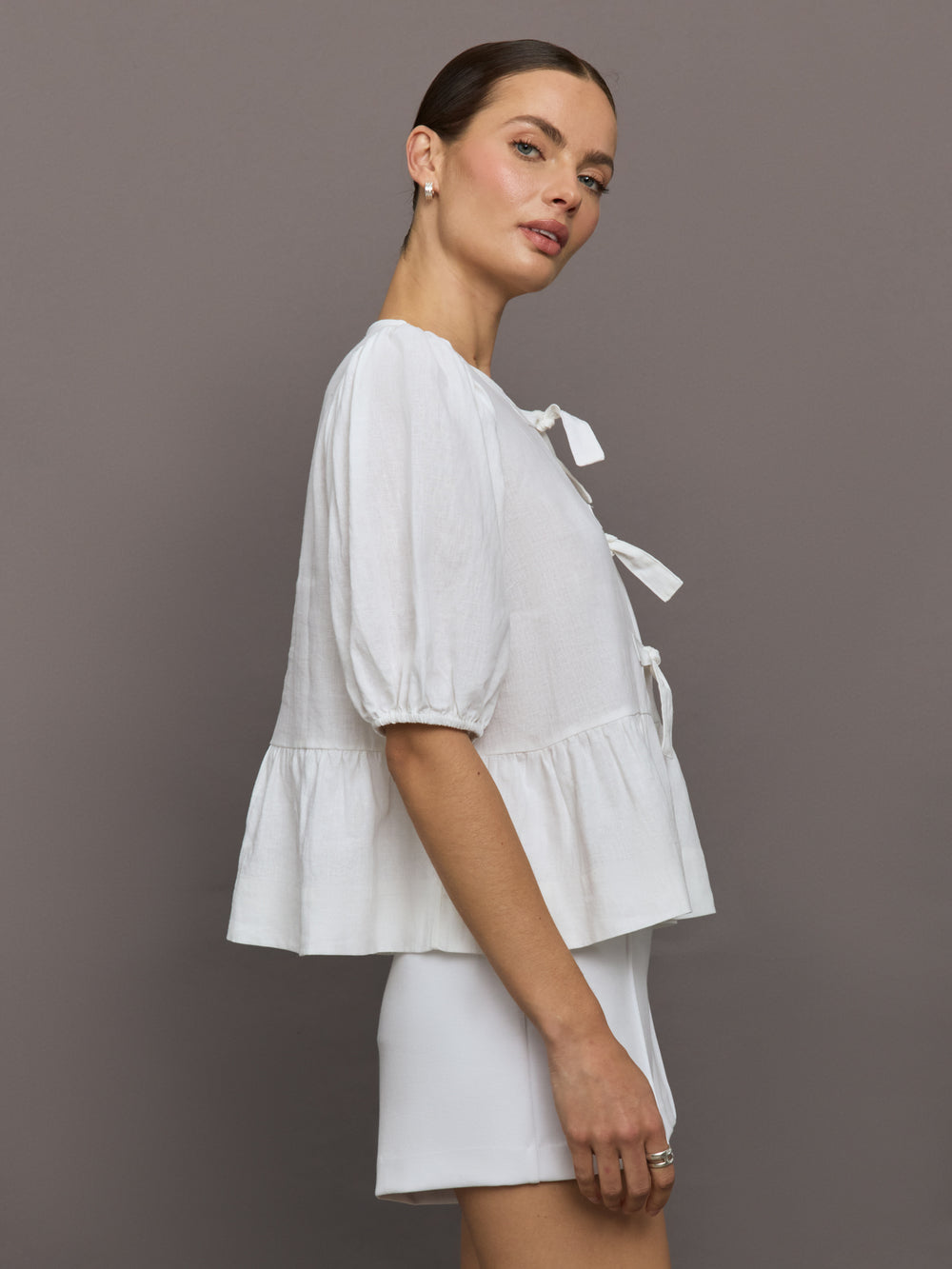 Model wears white puff sleeve top with a front ties and high neckline.
