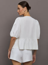 Model wears white puff sleeve top with a front ties and high neckline.
