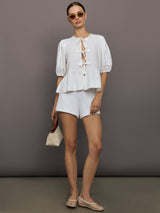 Model wears white puff sleeve top with a front ties and high neckline.

