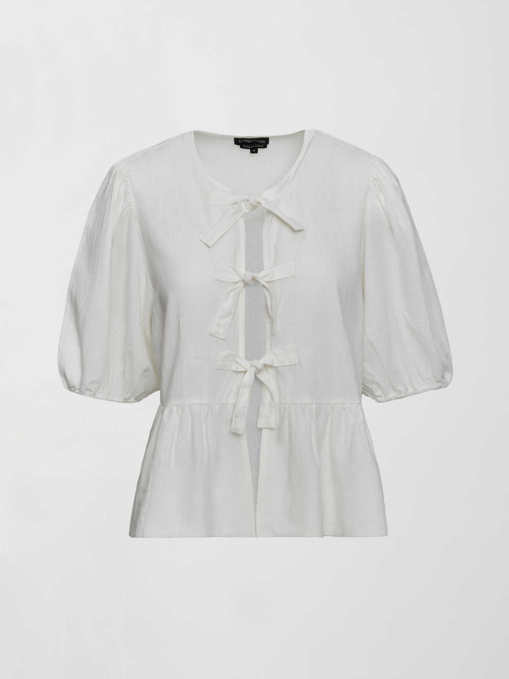 Model wears white puff sleeve top with a front ties and high neckline.
