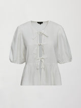 Model wears white puff sleeve top with a front ties and high neckline.
