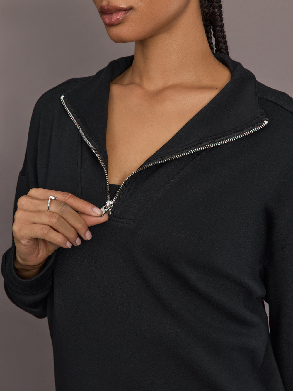 Model is wearing Interlock half zip pullover in black, close-up zipper detail.