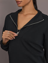 Model is wearing Interlock half zip pullover in black, close-up zipper detail.
