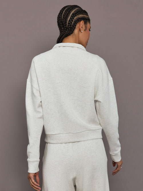 Model is wearing Interlock half zip pullover in Moonbeam Heather, back view.