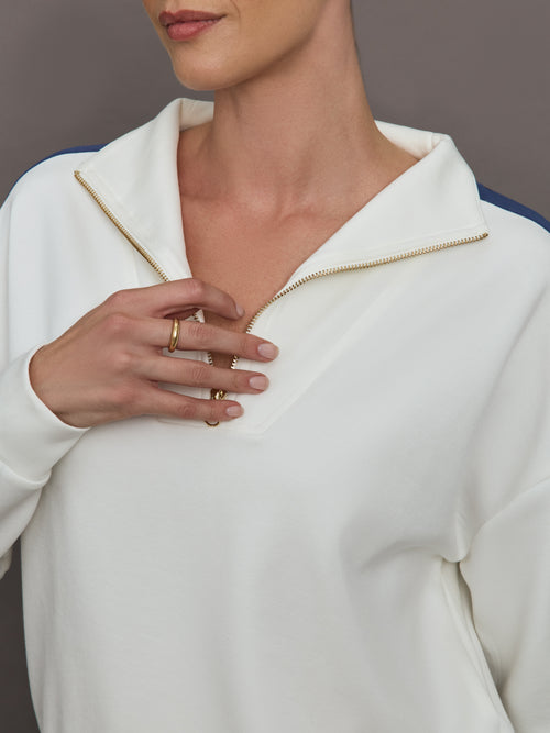 Model wearing an ivory half zip sweatshirt with blue accents.
