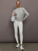 Full outfit view of grey bow embellished sweatshirt with jeweled shoulder bow, paired with white leggings, sneakers, and silver bag.