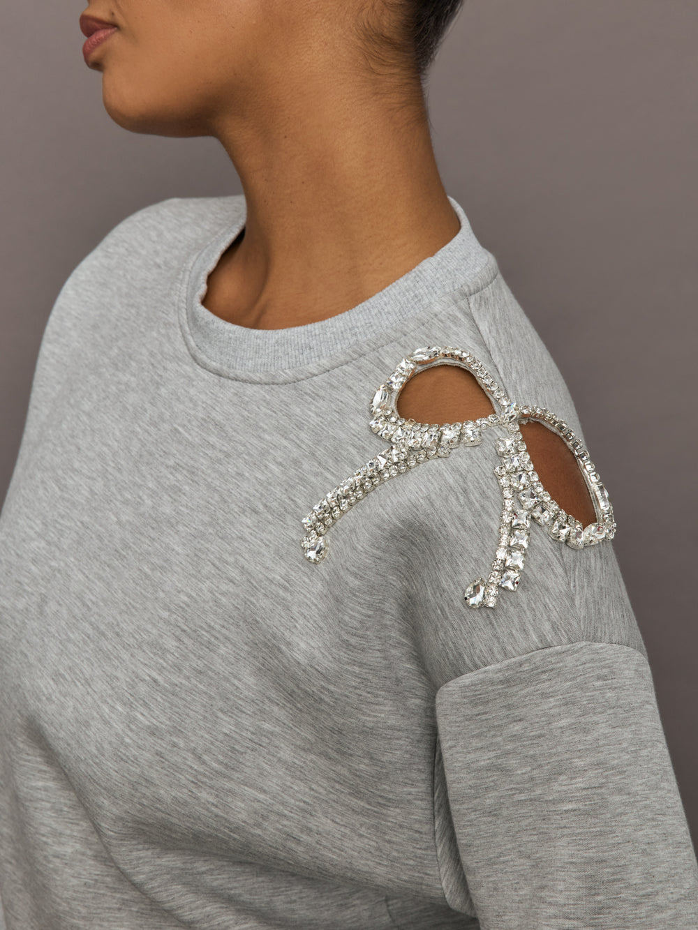 Close-up of grey bow embellished sweatshirt showing crystal bow detail on cutout shoulder.